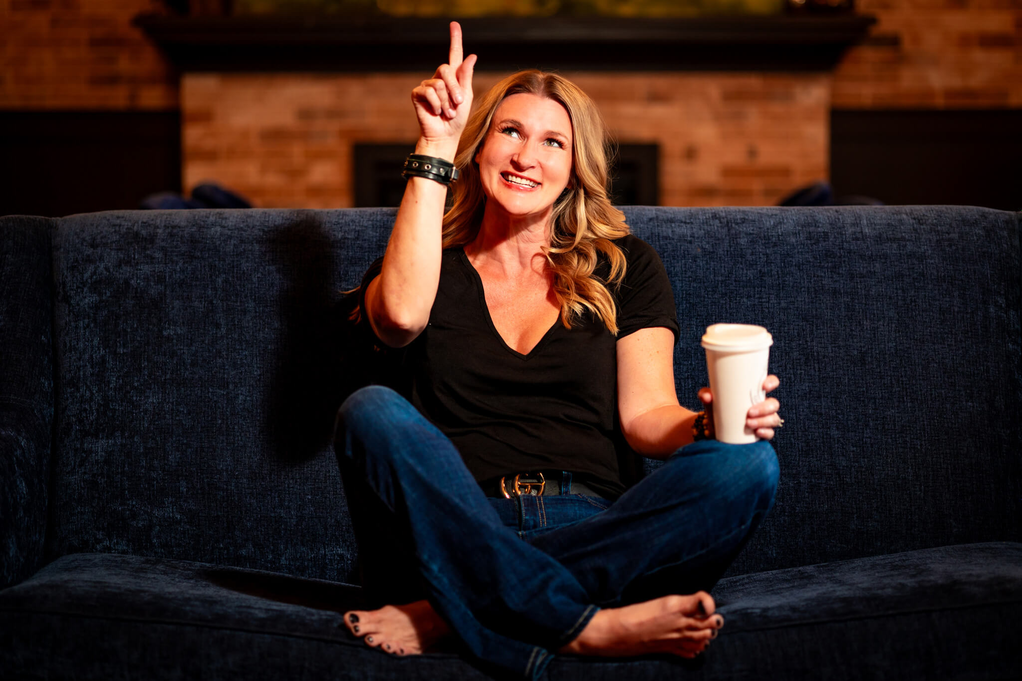 Callie Croken, a life and business coach, playfully pointing while sitting on a couch during her branding photoshoot with Lake Design.