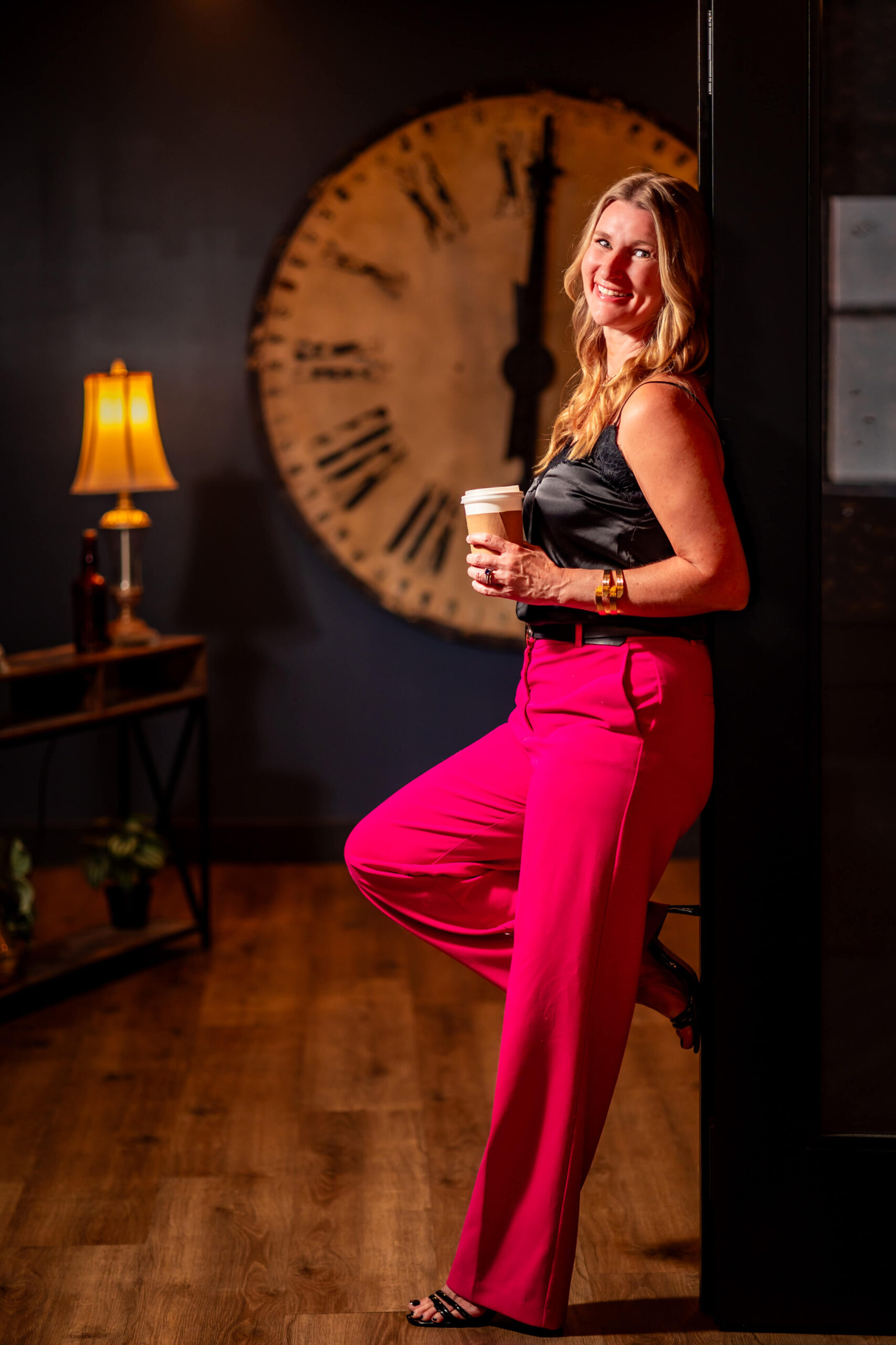 Callie Croken leaning against a wall with a clock in the background, holding a coffee cup during a branding photoshoot by Lake Design.